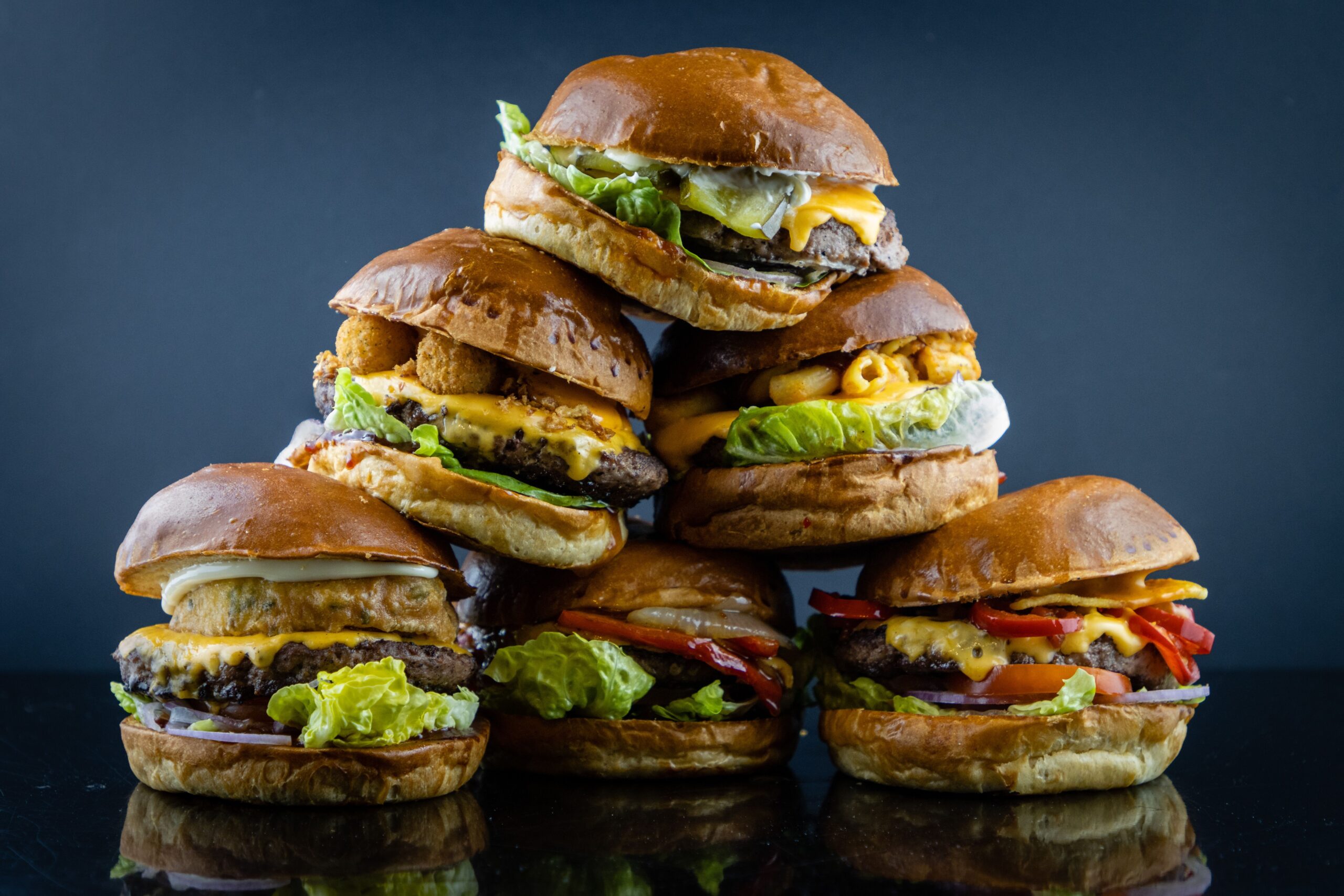 Delicious stack of assorted gourmet cheeseburgers photographed against a dark background.
